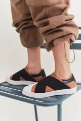 Zapatillas urbanas con diseño de bandas elásticas cruzadas en el empeine. Combinan cuero en tono tostado, detalles en negro y puntera blanca, con suela de goma blanca.