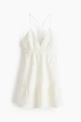 Vestido corto de muselina de algodón color blanco, de corte holgado con espalda abierta, escote en V y breteles finos cruzados. Cuenta con sección fruncida bajo el busto y un volado en el bajo.
