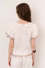 Blusa blanca de manga corta con detalles de bordados y perforaciones, cuello redondo y diseño holgado.