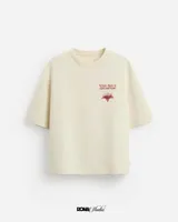 Remera color crudo de corte cuadrado, con cuello redondo y mangas cortas. Estampa en el frente con texto "Where there is dust and hope" y un dibujo de una casa.