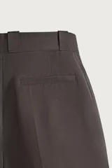 Bermuda de corte relaxed fit color marrón, con pliegues frontales, bolsillos laterales y detalle de bolsillos traseros de vivo, además de bolsillo cerillero. Cuenta con cierre frontal con cremallera y gancho metálico oculto.