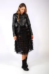 Chaqueta de cuero sintético negra con cierre frontal, solapas y cinturón integrado, combinada con una falda de tul con volados en capas.