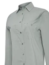 Blusa de manga larga con cuello camisero, confeccionada en una mezcla técnica de algodón orgánico, nylon y spandex. Presenta cierre frontal con botones, dos bolsillos frontales con solapa y paneles laterales reforzados. Cuenta con protección solar UPF 20+ integrada.