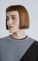 Buzo de cuello redondo con diseño oversize y corte crop. Confeccionado en frisa de algodón color gris melange, presenta un recorte asimétrico en color negro en microfibra con un bolsillo frontal funcional con cierre a presión.