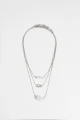 Collar triple de cadena fina plateada, con tres niveles de largo. El primer nivel presenta un dije cilíndrico blanco, el segundo un dije de mosquetón metálico y el tercero un dije de piedra blanca ovalada.