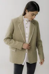 Blazer color camel de lana con solapas y cierre con botones. Presenta detalle de pespuntes blancos en los bordes.