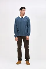 Remera polo de manga larga en color azul, confeccionada en algodón pesado con textura suave. Presenta cuello camisero en color crema, cierre frontal con botones y puños en las mangas. Incluye un pequeño bordado en el pecho.