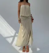 Vestido largo color beige, sin tirantes, con escote recto y detalle fruncido en la cintura. La falda es fluida y tiene una abertura lateral.