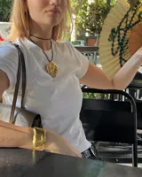 Collar con dije grande de bronce con forma orgánica y textura rugosa, suspendido de un cordón negro. Incluye cordones intercambiables.