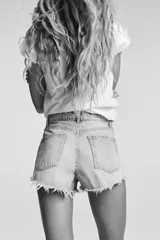 Short de jean negro desgastado, tiro alto, con roturas pronunciadas y terminación deshilachada en el bajo. Presenta cinco bolsillos y cierre frontal con botón metálico.