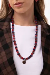 Collar largo compuesto por cuentas rectangulares de acrílico en color rojo y piedras naturales en tono azul oscuro, con un dije circular central pintado a mano. Incluye cadena de acero quirúrgico para ajuste de largo.