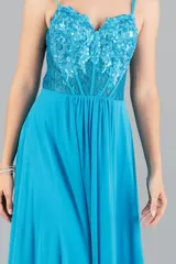 Vestido largo de fiesta color turquesa, con cuerpo tipo corset bordado con lentejuelas y transparencias, tirantes finos y falda fluida con tajo lateral.
