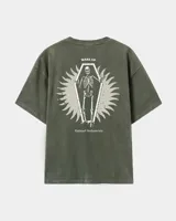Remera oversize de color marrón topo con efecto acid wash, cuello redondo y manga corta. Cuenta con un pequeño estampado gráfico frontal con el texto 'WAKE UP IND' y una calavera.