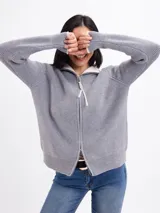 Campera de tejido de punto en color gris, con cierre frontal completo y cuello alto. Presenta un diseño de canalé vertical y puños con detalle en contraste.