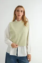 Chaleco de punto color verde salvia, con cuello redondo y diseño sin mangas. Presenta detalles de pedrería brillante y pequeños apliques decorativos distribuidos por toda la prenda.