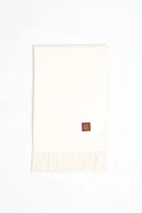 Pashmina de textura suave en color blanco, con flecos en los extremos y un pequeño parche de cuero sintético marrón con logo grabado.