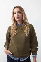 Sweater de tejido suave color tostado, con cuello redondo y detalle de flores bordadas en relieve en la parte superior del pecho. Presenta un corte relajado y mangas largas con puños ajustados.