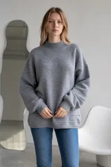 Sweater de punto color crema, con cuello alto y diseño holgado. Presenta puños y ruedo acanalados con detalle de líneas horizontales en la parte inferior.