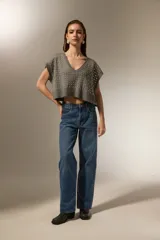 Chaleco de punto gris con cuello en V, diseño sin mangas y corte cropped. Presenta apliques de tachas metálicas plateadas distribuidas por toda la parte frontal y borde acanalado en el ruedo.