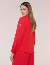 Blusa azul de corte holgado y fluido, con escote en V y mangas largas raglán que presentan detalles de calados con forma de flores y puños elastizados.