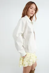 Campera bomber color beige con cuello solapa, confeccionada en 100% algodón, con cierre frontal con cremallera y acabado elástico en el bajo.