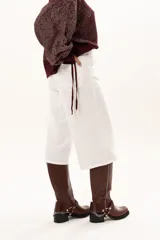 Bermuda de corte recto y tiro alto, confeccionada en gabardina blanca, con cierre frontal de botón y cremallera, y bolsillos laterales.