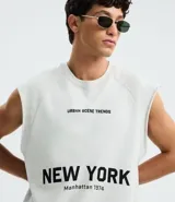 Musculosa masculina de corte boxy fit, confeccionada en algodón. Presenta cuello redondo, hombros ligeramente ampliados y acabado deshilachado en el ruedo. Cuenta con estampa frontal con la frase 'Urban Scene Trends' y el texto 'New York Manhattan 1974' en el centro.