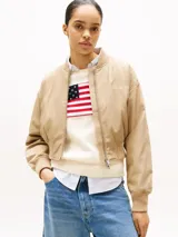 Campera bomber corta de color beige, con cierre frontal, cuello estilo béisbol, puños y bajo de punto canalé. Presenta un logo bordado en el pecho.