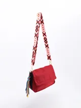 Bandolera de diseño rectangular con solapa frontal, confeccionada en material sintético de acabado liso. Incluye un detalle decorativo lateral compuesto por cordones trenzados multicolor con punteras.