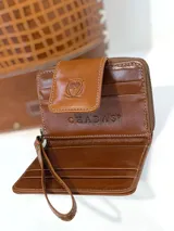 Mini billetera de cuero con diseño de pelo animal print en tonos marrón y blanco. Presenta un cierre de solapa con broche y un logo de búho grabado en el frente, además de una correa de muñeca extraíble.