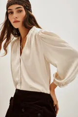 Camisa de satén color crema con escote en V, mangas largas abullonadas con puños elásticos y detalle de frunces en los hombros.