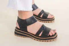 Sandalias de cuero negras con tiras cruzadas y ajuste al tobillo. Suela track color caramelo.