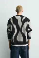 Cárdigan de punto con acabado cepillado, diseño de jacquard con patrón abstracto de ondas en gris y negro, cuello en pico, manga larga y cierre frontal con botones.