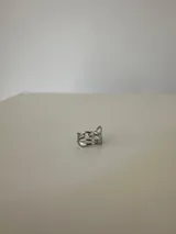 Anillo de diseño abierto y ajustable, con líneas curvas y orgánicas que se entrelazan, fabricado en acero quirúrgico.