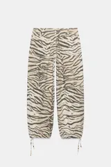 Pantalón de tiro medio con estampado animal print tipo tigre en tonos beige y negro. Presenta trabillas, cintura ajustable con cordones, bolsillos laterales y traseros, y bajo ajustable con cordón. Cierre frontal con cremallera y botón a presión.