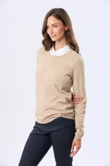 Buzo tejido en hilo de algodón color beige, con cuello redondo y manga larga. Presenta un corte clásico y un pequeño detalle metálico en la parte inferior izquierda.