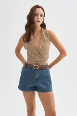 Top de punto con lentejuelas en tonos beige y dorado, con escote halter cruzado en V, sin mangas y corte corto.