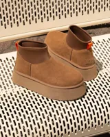 Botas cortas tipo plataforma UGG modelo Mini Dipper, confeccionadas en gamuza color tostado con panel superior de neopreno elástico y tirador naranja en el talón.