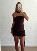 Vestido corto marrón oscuro, estilo strapless, con detalle de frunces en la cintura y falda con volados superpuestos. Incluye un accesorio tipo choker o corbatín a juego.