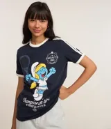 Remera azul marino de algodón con cuello redondo y mangas cortas con rayas blancas en los hombros. Estampado frontal de la Pitufina jugando al tenis.