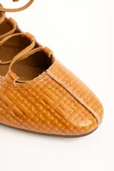 Zapatos planos de cuero color caramelo, con textura trenzada, cordones frontales en el empeine y punta redondeada.