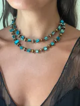 Collar doble de estilo artesanal, compuesto por cuentas de nácar teñidas en color turquesa, intercaladas con discos metálicos en tonos dorado y plateado y mostacillas. Presenta un diseño de doble hilera y cierre con cadena de extensión.