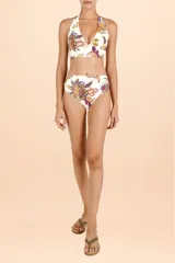 Top de bikini estilo halter con escote profundo y banda ancha bajo el busto. Presenta un diseño estampado con motivos botánicos y paisley en tonos cálidos y púrpura sobre fondo blanco.