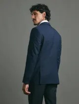 Saco de vestir azul marino con cuello solapa, manga larga y cierre frontal de dos botones. Presenta un diseño clásico con bolsillos laterales con solapa y un bolsillo superior en el pecho.