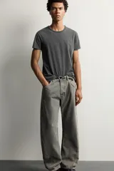 Jeans loose fit de hombre en denim de algodón color gris oscuro con efecto lavado. Presenta perneras con costuras giradas hacia los tobillos, tiro medio, cierre frontal con botones y bolsillos frontales con bolsillo cerillero.