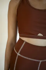 Top deportivo color ladrillo de lycra reciclada con breteles cruzados y detalle de abertura en forma de medialuna en el delantero inferior.