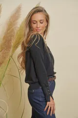 Buzo tejido color negro, de manga larga, escote en V y tajitos en ambos costados. Presenta puños con detalle de tres botones dorados.