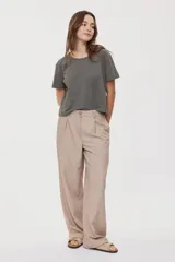 Pantalón sastrero beige de pierna amplia, tiro medio, con cintura con pasacintos, pinzas delanteras y cierre frontal con botón y cremallera.