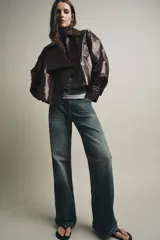 Chaqueta de Zara Woman Collection en tejido con acabado brillante efecto cuero. Presenta cuello solapa, manga larga con trabillas ajustables, bolsillos delanteros y cierre frontal con botones ocultos bajo solapa.