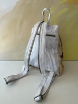 Mochila Lucy de cuero blanco y detalles dorados, con diseño de arte pintado a mano en el bolsillo frontal, cierre superior y correas ajustables.